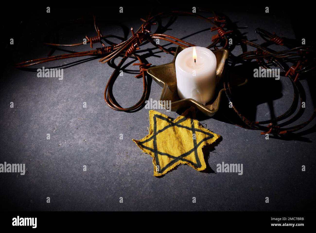 Holocaust-Gedächtnisfeiertag. Stacheldraht-Stern und brennende Kerze auf schwarzem Hintergrund Stockfoto