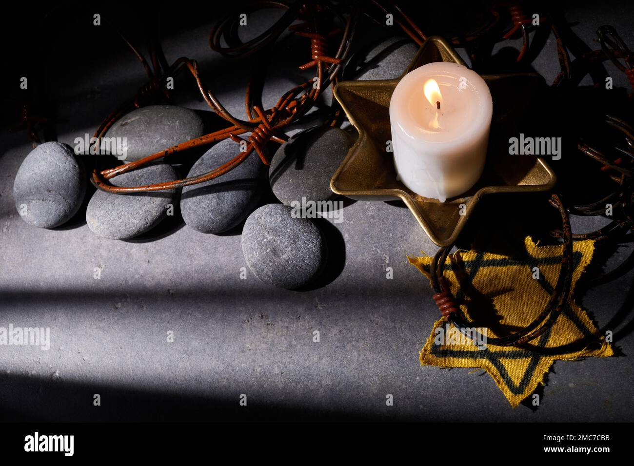 Holocaust-Gedächtnisfeiertag. Stacheldraht, Steine, gelber Stern und brennende Kerze auf schwarzem Hintergrund Stockfoto