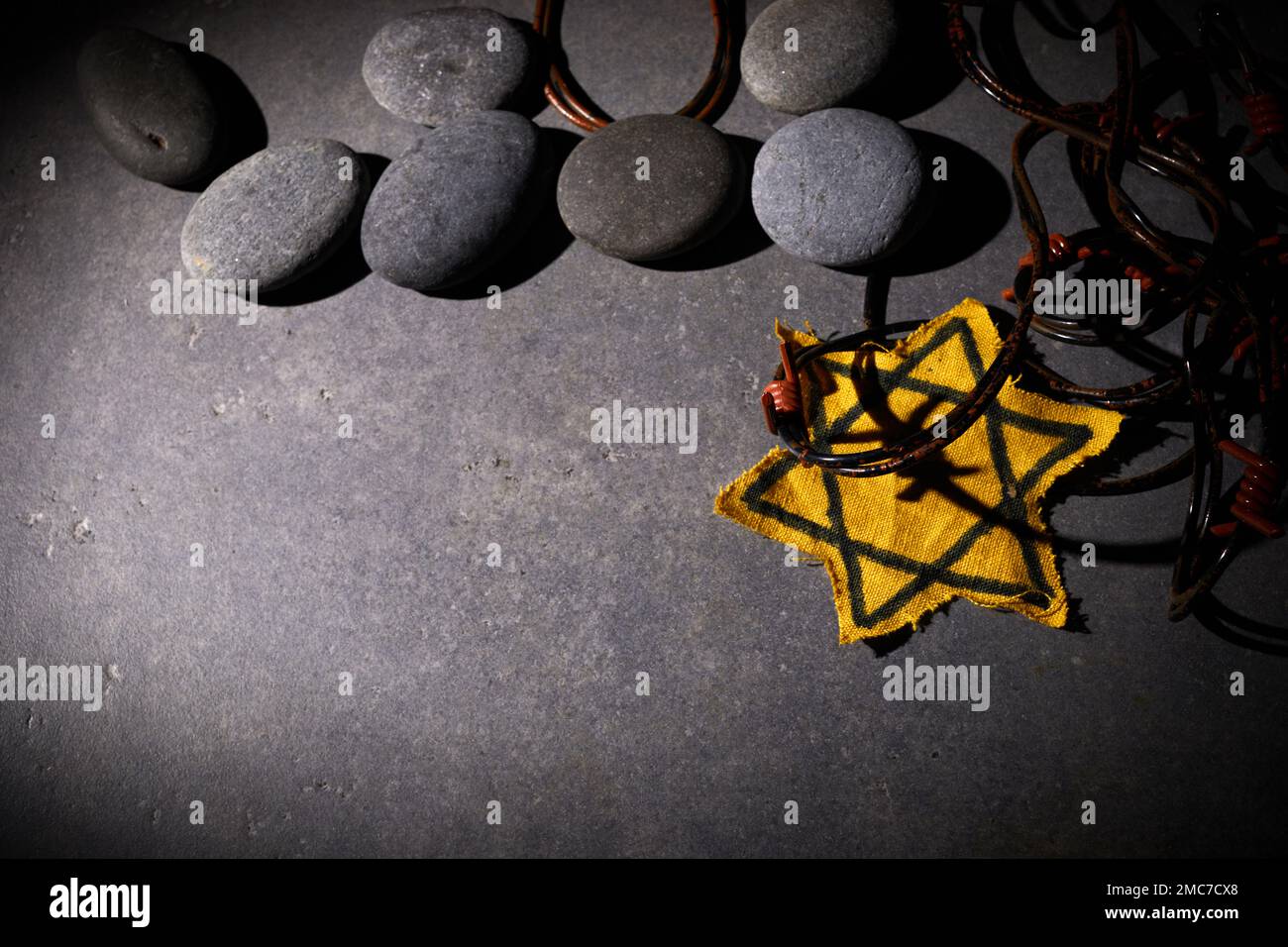 Holocaust-Gedächtnisfeiertag. Stacheldraht, Steine und gelber Stern auf dunklem Hintergrund Stockfoto