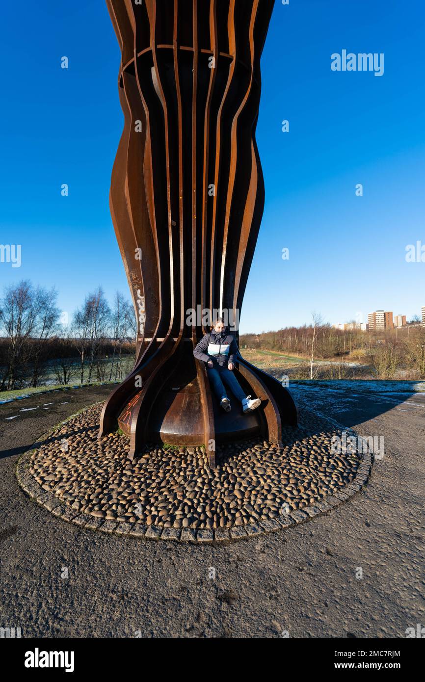 Engel des Nordens, Gateshead, Tyne and Wear, UK von Anthony Gormley, mit einer jungen Frau oder einem Mädchen, die auf den Füßen der Statue sitzt Stockfoto
