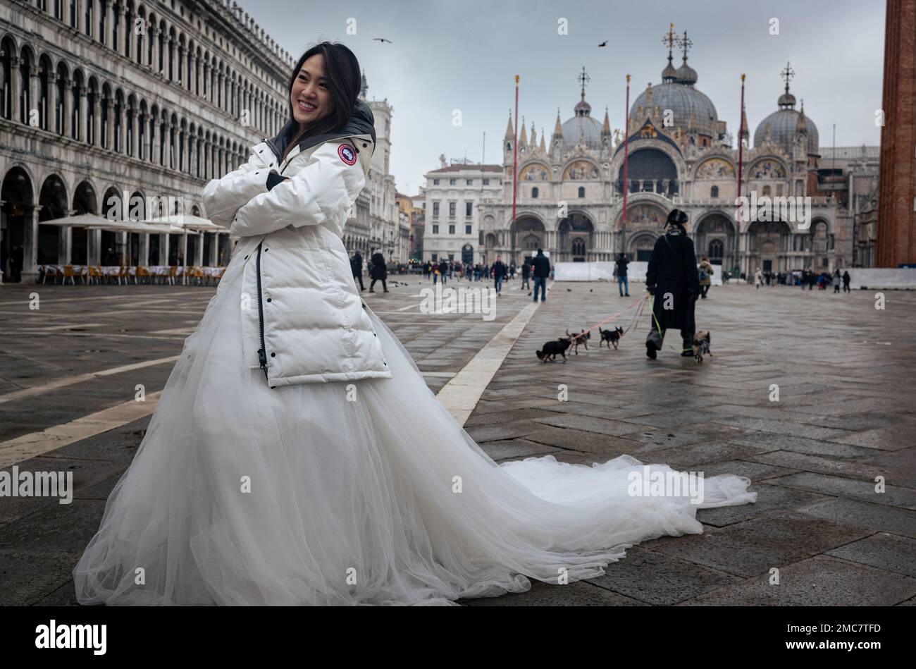 18. Januar 2023, Venedig Italien. Eine wunderschöne Asiatin, die ein Hochzeitskleid und einen weißen Wintermantel trägt, posiert auf der Piazza San Marco. Stockfoto