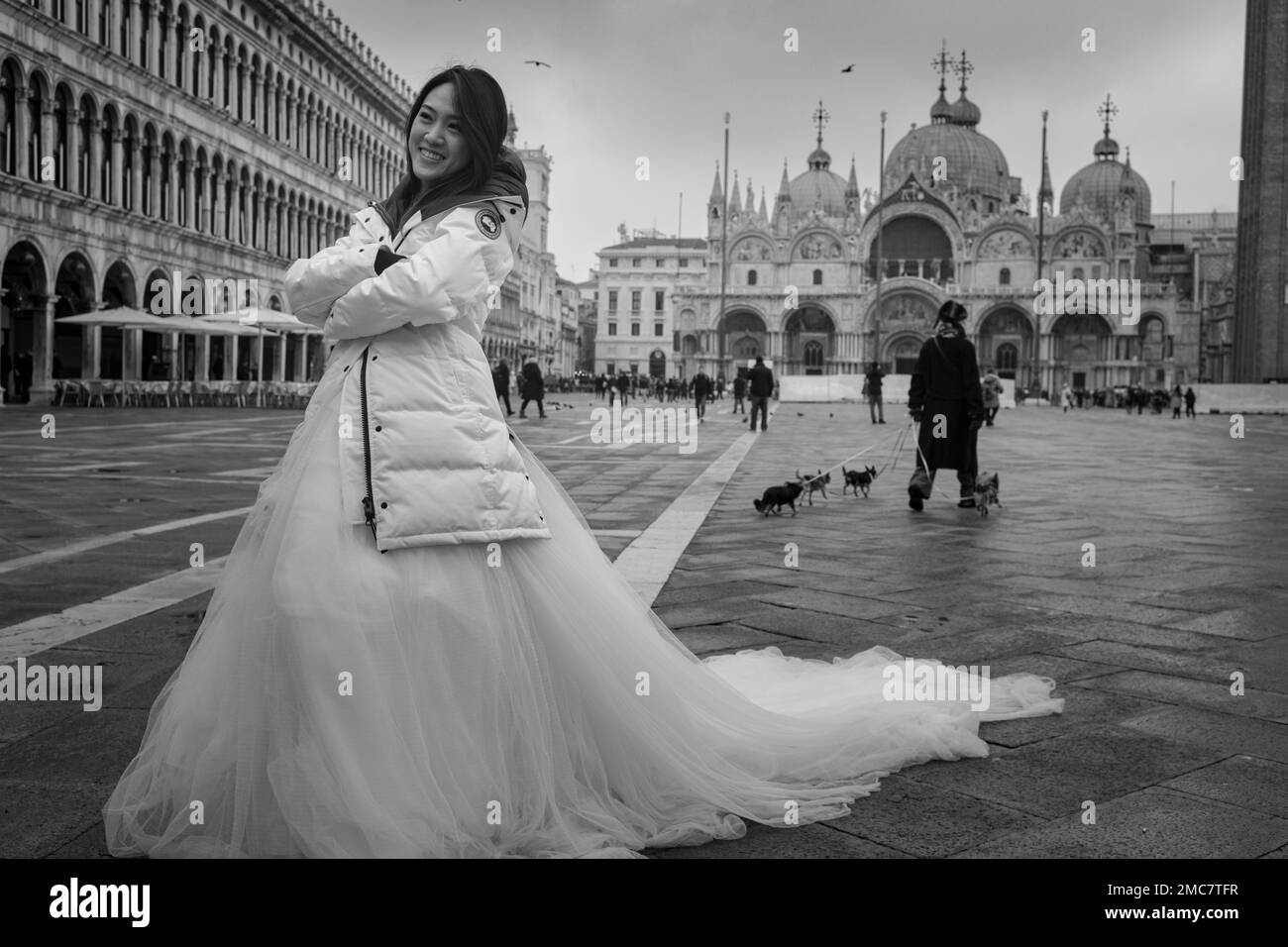 18. Januar 2023, Venedig Italien. Eine wunderschöne Asiatin, die ein Hochzeitskleid und einen weißen Wintermantel trägt, posiert auf der Piazza San Marco. Stockfoto