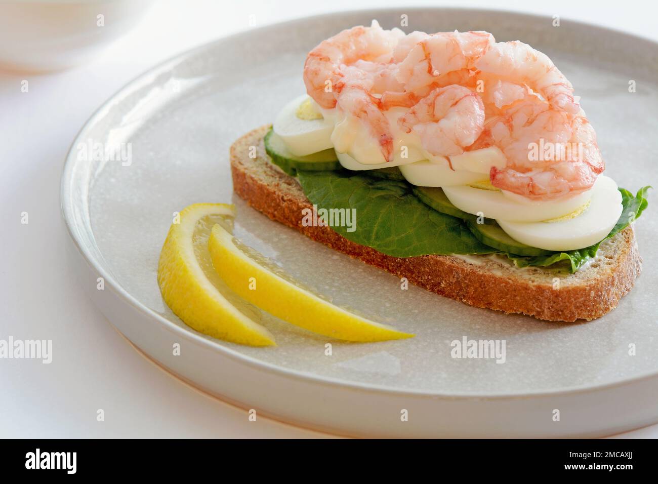 Frisches und gesundes Shrimp- und Ei-Sandwich auf Roggenbrot, mit Zitronenkeilen in horizontaler Form. Traditionelle skandinavische Smorrebrod. Stockfoto
