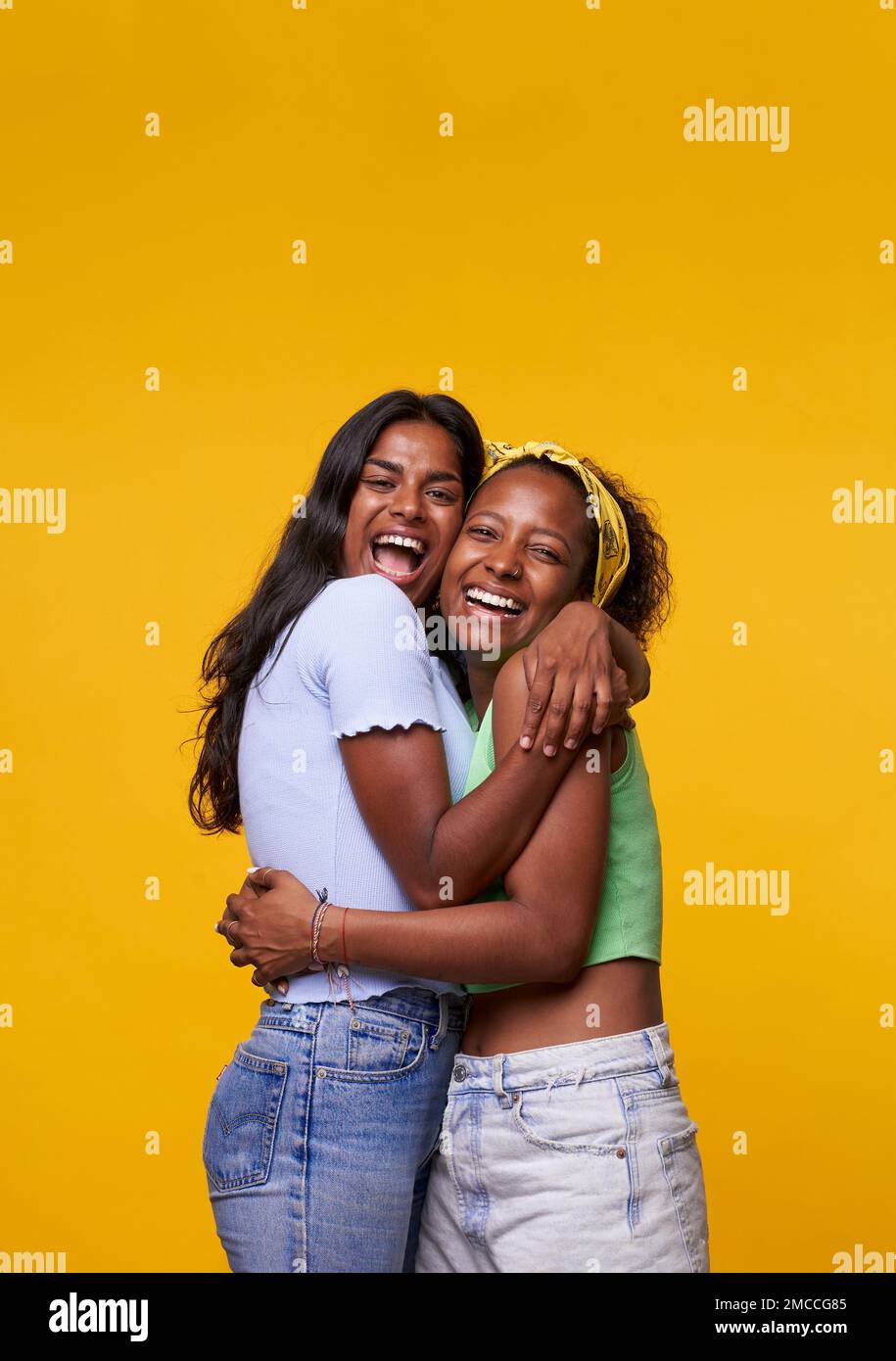 Vertikal. Zwei Diversität ziemlich positive Mädchen mit einem Lächeln, isoliert auf gelbem Hintergrund. Stockfoto
