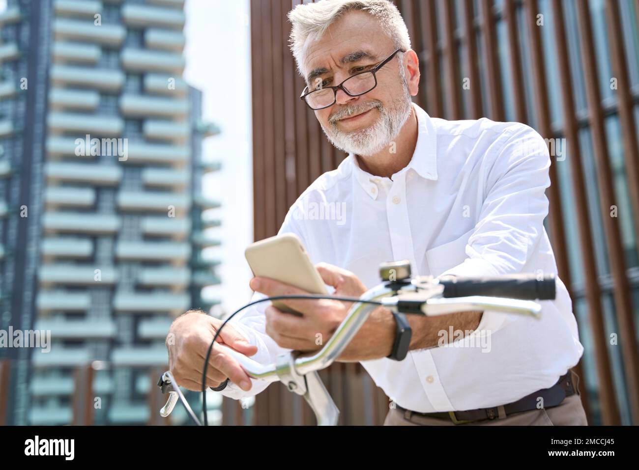 Älterer aktiver Mann, der ein Mobiltelefon benutzt und ein Fahrrad in der App ausmietet, um in der Stadt zu fahren. Stockfoto