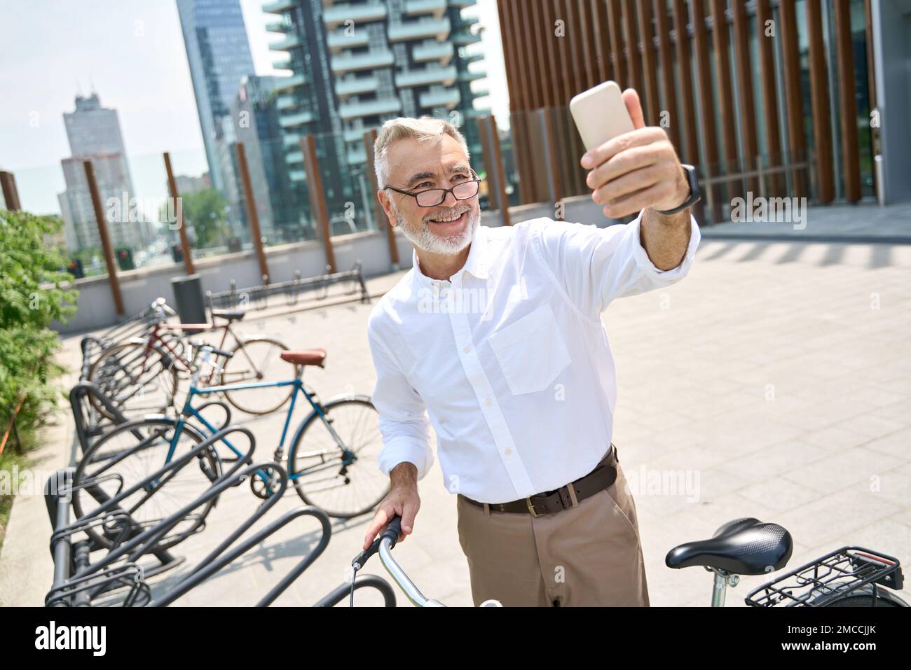Glücklicher älterer Mann, der ein Telefon mietete und Fahrrad mietete, um in der Stadt Fahrrad zu fahren. Stockfoto