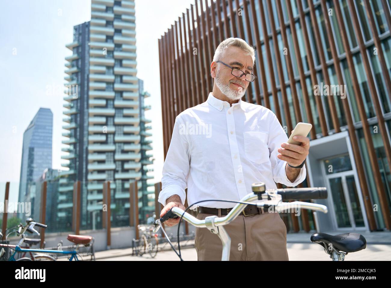 Ein älterer Mann, der sein Handy in einer Leihanwendung für Fahrräder im Stadtpark mietet. Stockfoto