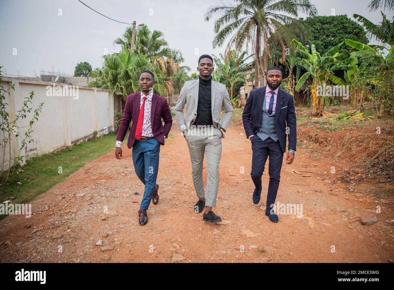 Drei afrikanische Gentlemen gehen eine unbefestigte Straße entlang, elegant gekleidete Leute Stockfoto