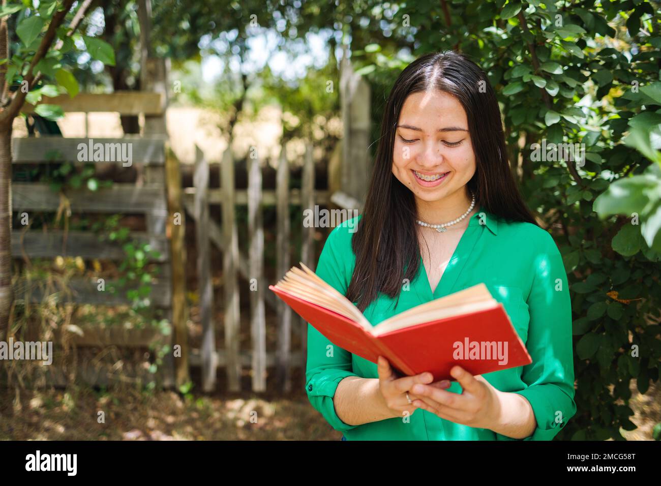 Lächelnde junge Farmerin, die auf dem Feld ein Buch liest. Vertikaler Schuss. Weltbuchtag. Speicherplatz kopieren Stockfoto