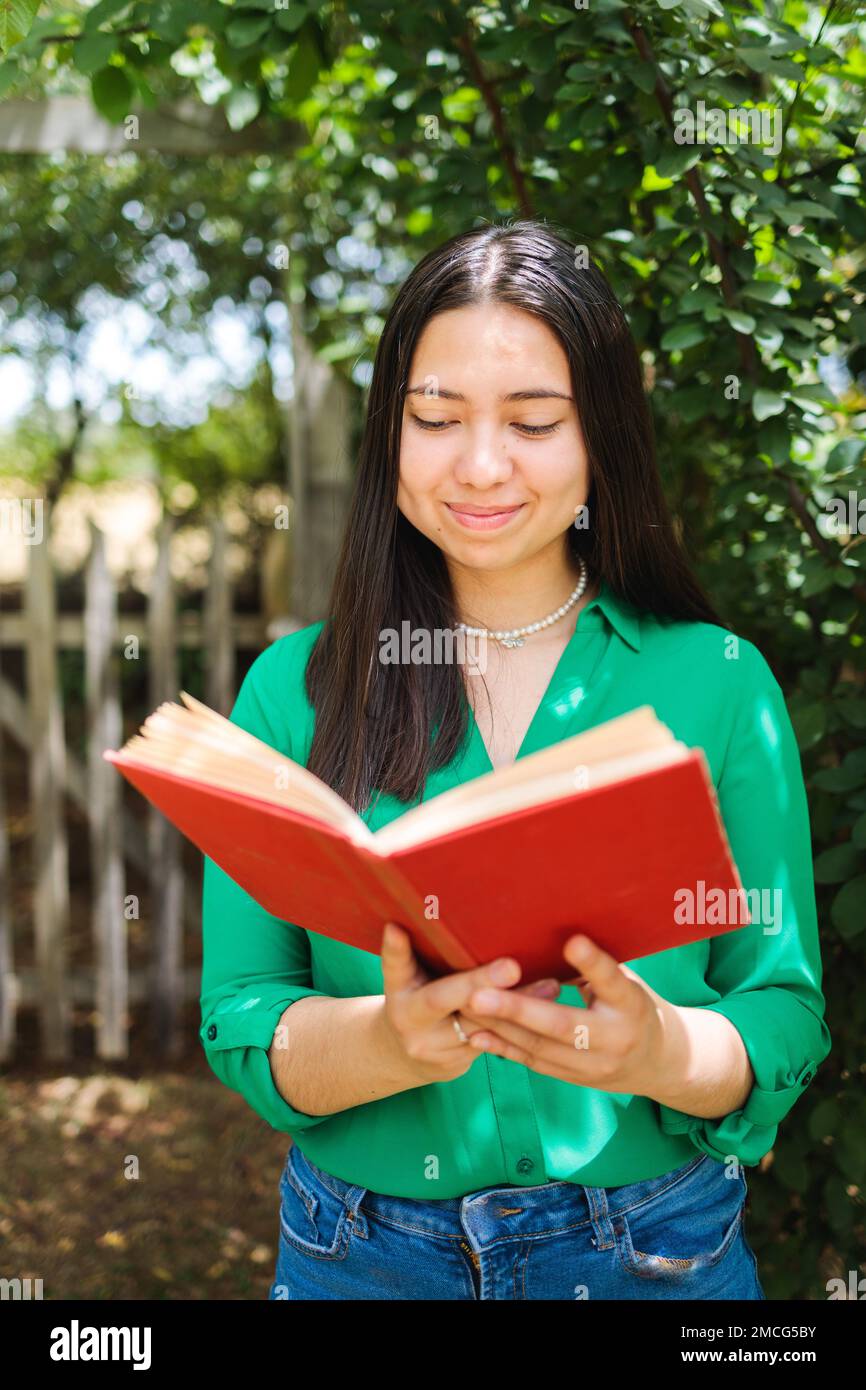 Eine schöne lächelnde junge Farmerin, die auf dem Feld ein Buch liest. Vertikaler Schuss. Weltbuchtag Stockfoto