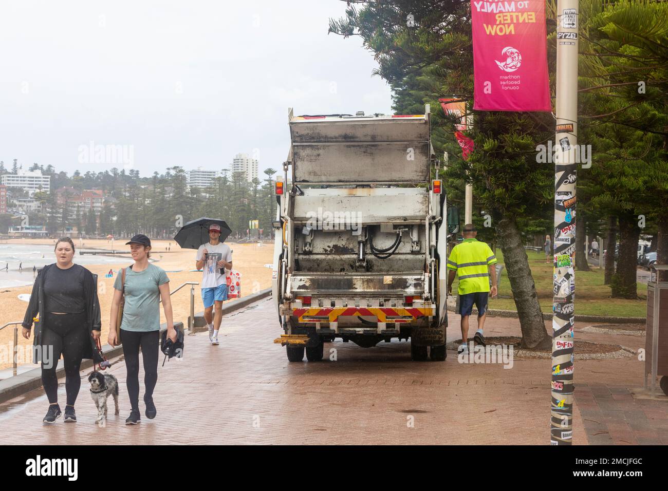 Müllwagen und gemeindefahrer, die öffentliche Mülltonnen leeren, Manly Beach Promenade, Sydney, NSW, Australien nasses Wetter Stockfoto