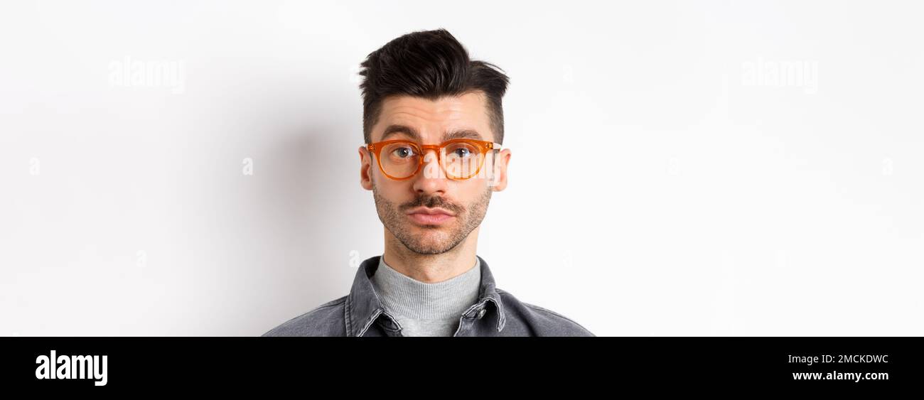 Attraktive Brünette Mann mit Schnurrbart, trägt stilvolle Brille und sehen ernst an der Kamera, keine Emotion pokerface, vor weißem Hintergrund stehen Stockfoto