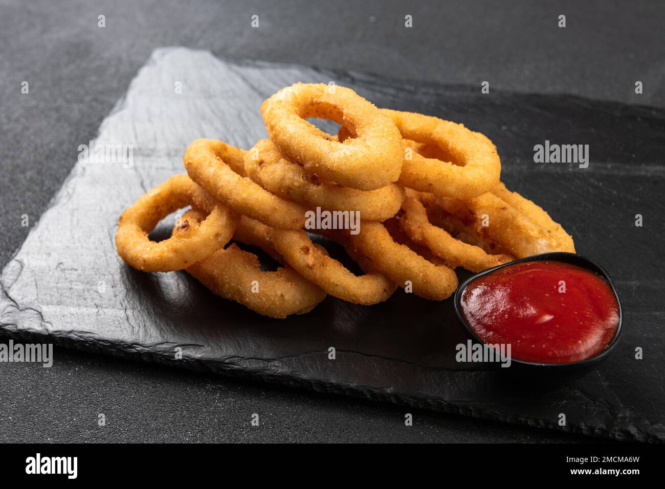Calamari-Ringe frittiert in Panade. Knusprige Tintenfischringe auf dunklem Hintergrund mit Sauce. Stockfoto