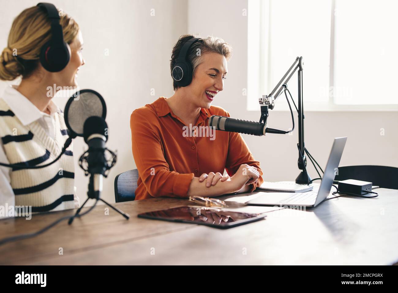 Fröhliche Podcaster, die eine gute Zeit haben, während sie eine Audioübertragung in einem Heimstudio moderieren. Lächelnde Content-Ersteller, die einen Internet-Podcast aufzeichnen Stockfoto