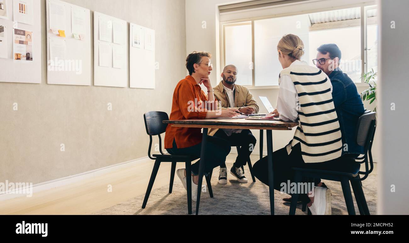 Gruppe kreativer Geschäftsleute, die während eines Meetings in einem modernen Büro Brainstorming durchführen. Verschiedene Konstrukteure diskutieren, während sie gemeinsam an einem arbeiten Stockfoto