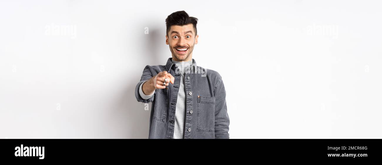 Du bist es. Aufgeregt lächelnden Mann zeigt Finger auf die Kamera mit fröhlichem Gesicht, erkennen Person, stehend in Denim Jacke auf weißem Hintergrund Stockfoto
