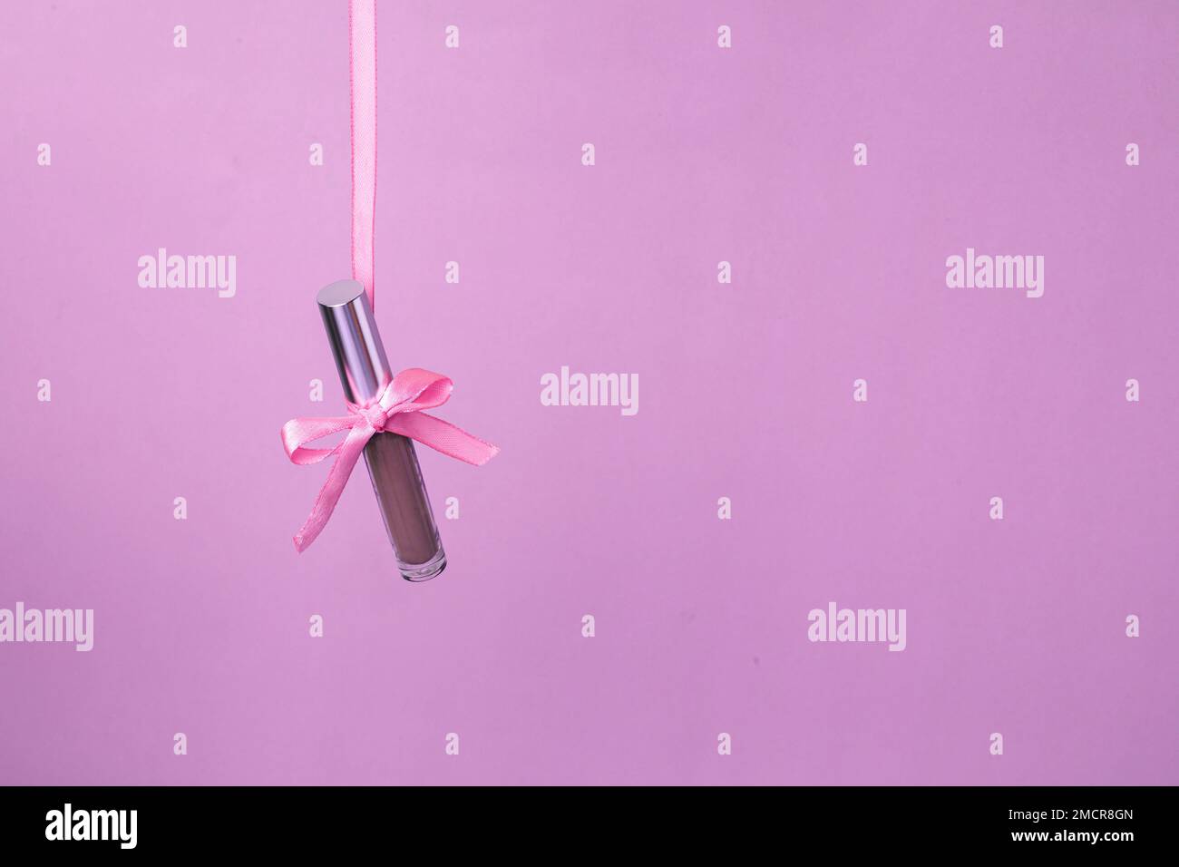 Flüssiger Schatten mit natürlichem Farbton hängt auf einem pinkfarbenen Band auf pinkfarbenem Hintergrund. Konzept des Geschenks für Frauen oder St. Valentinstag Stockfoto