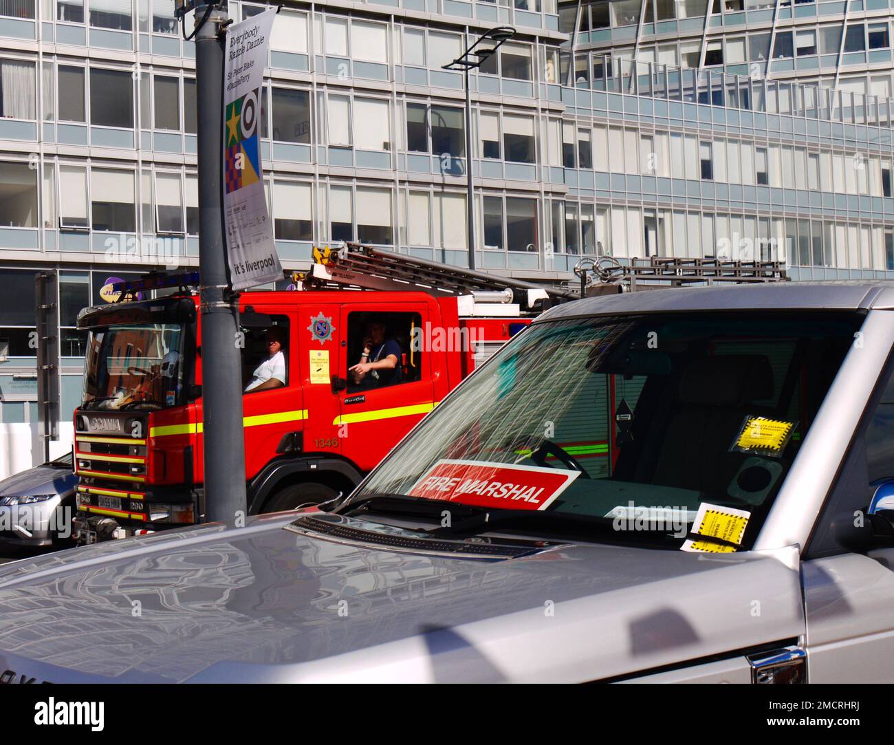 Feuerwehrmänner in einem vorbeifahrenden Feuerwehrwagen schauen, wie ein Fahrzeug eines Feuerwehrmanns zwei Strafzettel erhalten hat. Liverpool, Großbritannien Stockfoto