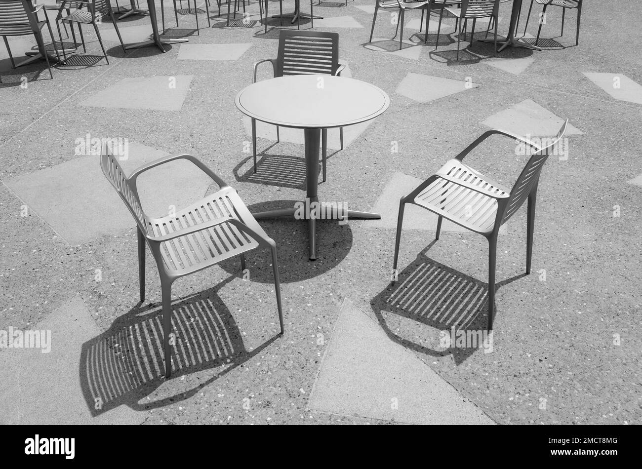 Schwarzweißfoto von Stühlen an einem leeren Tisch. Stockfoto