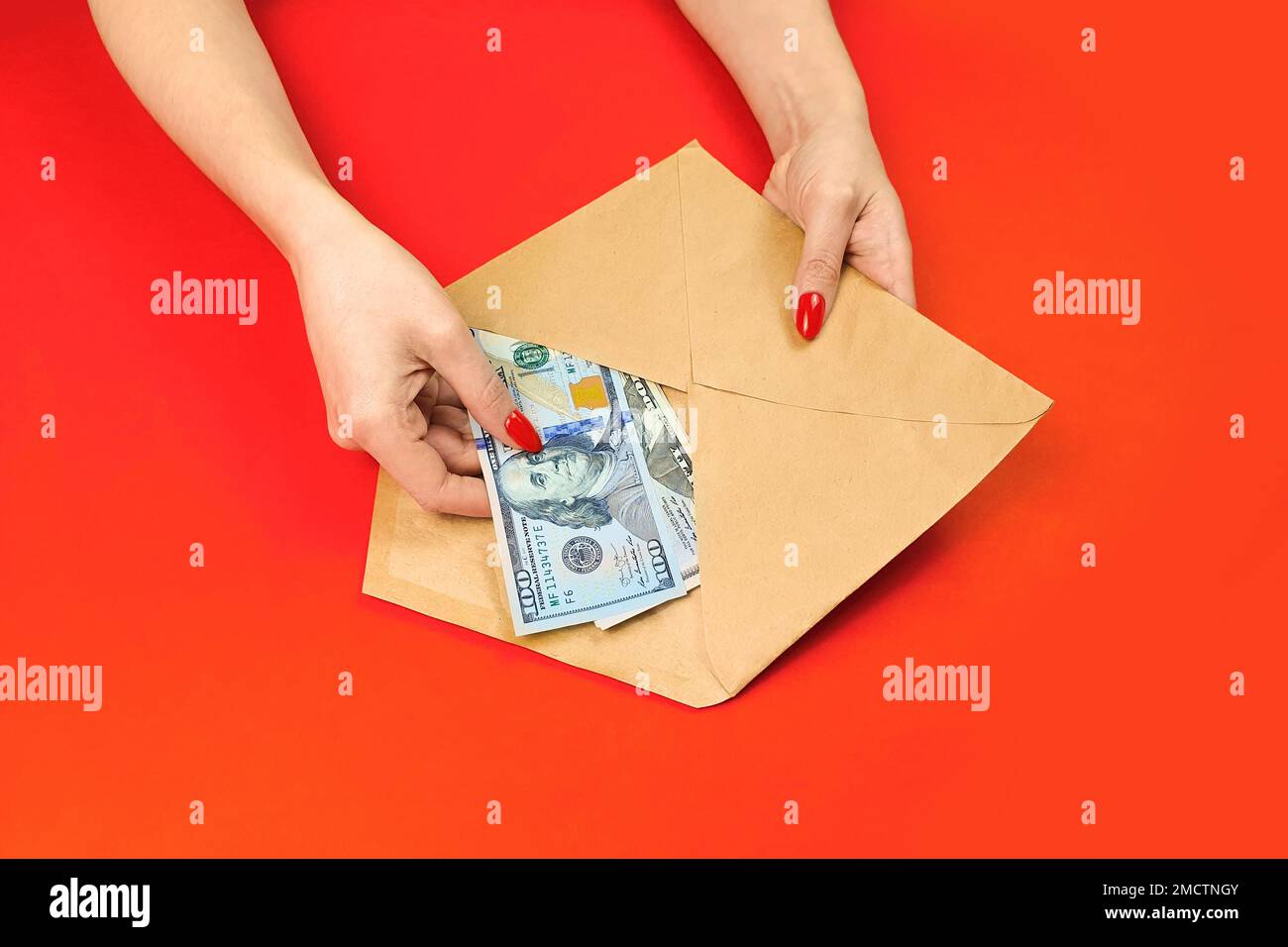 Weibliche Hände halten handwerkliche Umschläge mit Dollarscheinen, amerikanisches Geld auf dem roten Tisch. Draufsicht. Stockfoto