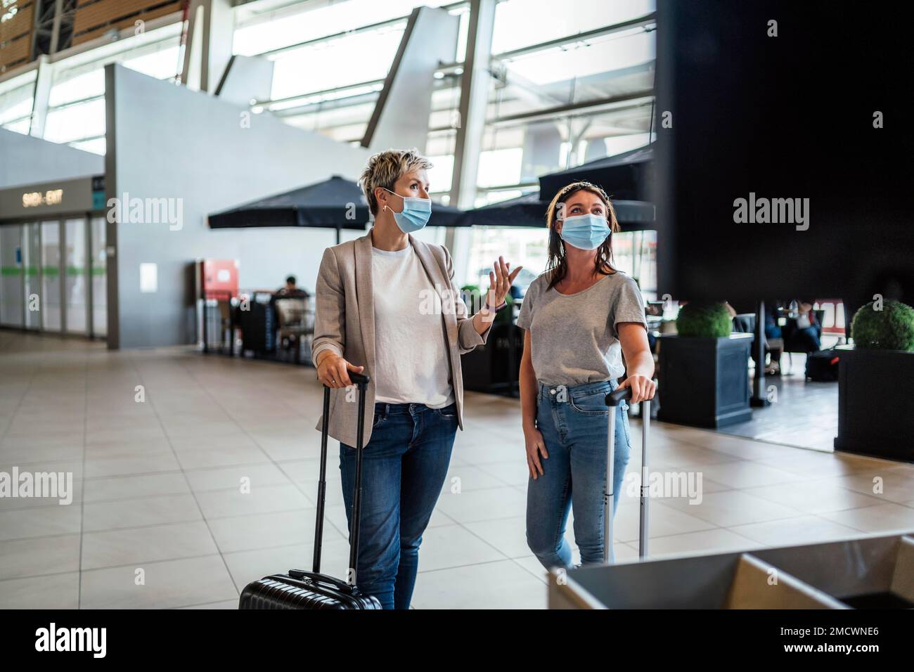 Zwei Reisende Frauen tragen Schutzmasken und diskutieren am Flughafen Faro über das Fluginformationsbrett Stockfoto