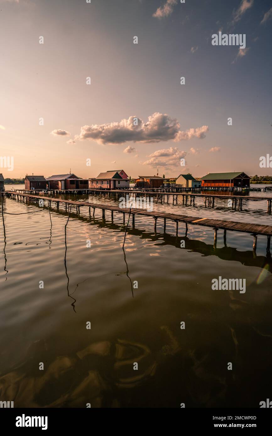 Kleine Holzhäuser mit einem Steg in einem See dienen als Angeln- und Ferienhäuser für Ungarn. Wunderschönes Landschaftsfoto bei Sonnenuntergang, Lake Bokodi Stockfoto