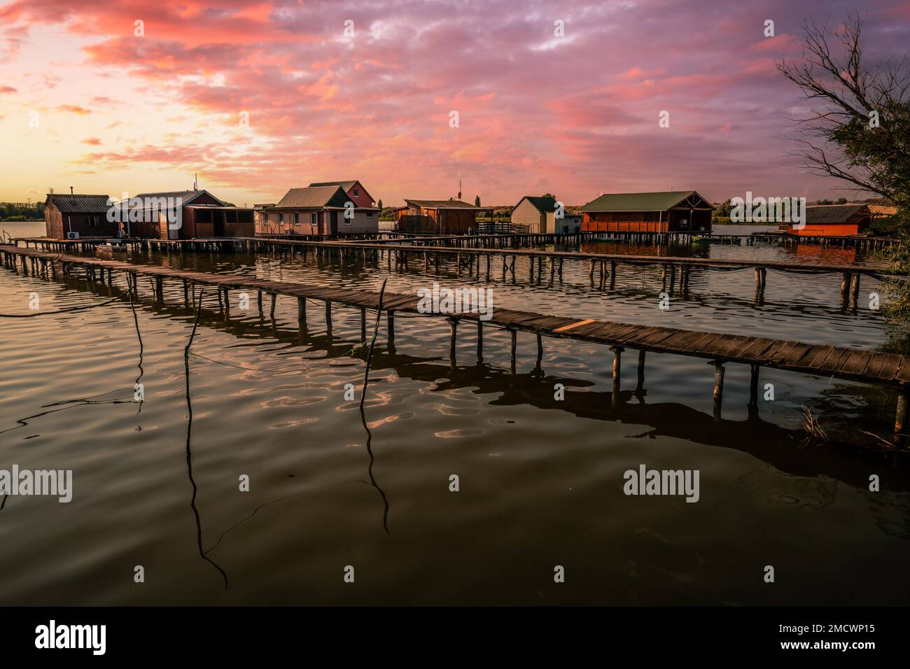 Kleine Holzhäuser mit einem Steg in einem See dienen als Angeln- und Ferienhäuser für Ungarn. Wunderschönes Landschaftsfoto bei Sonnenuntergang, Lake Bokodi Stockfoto