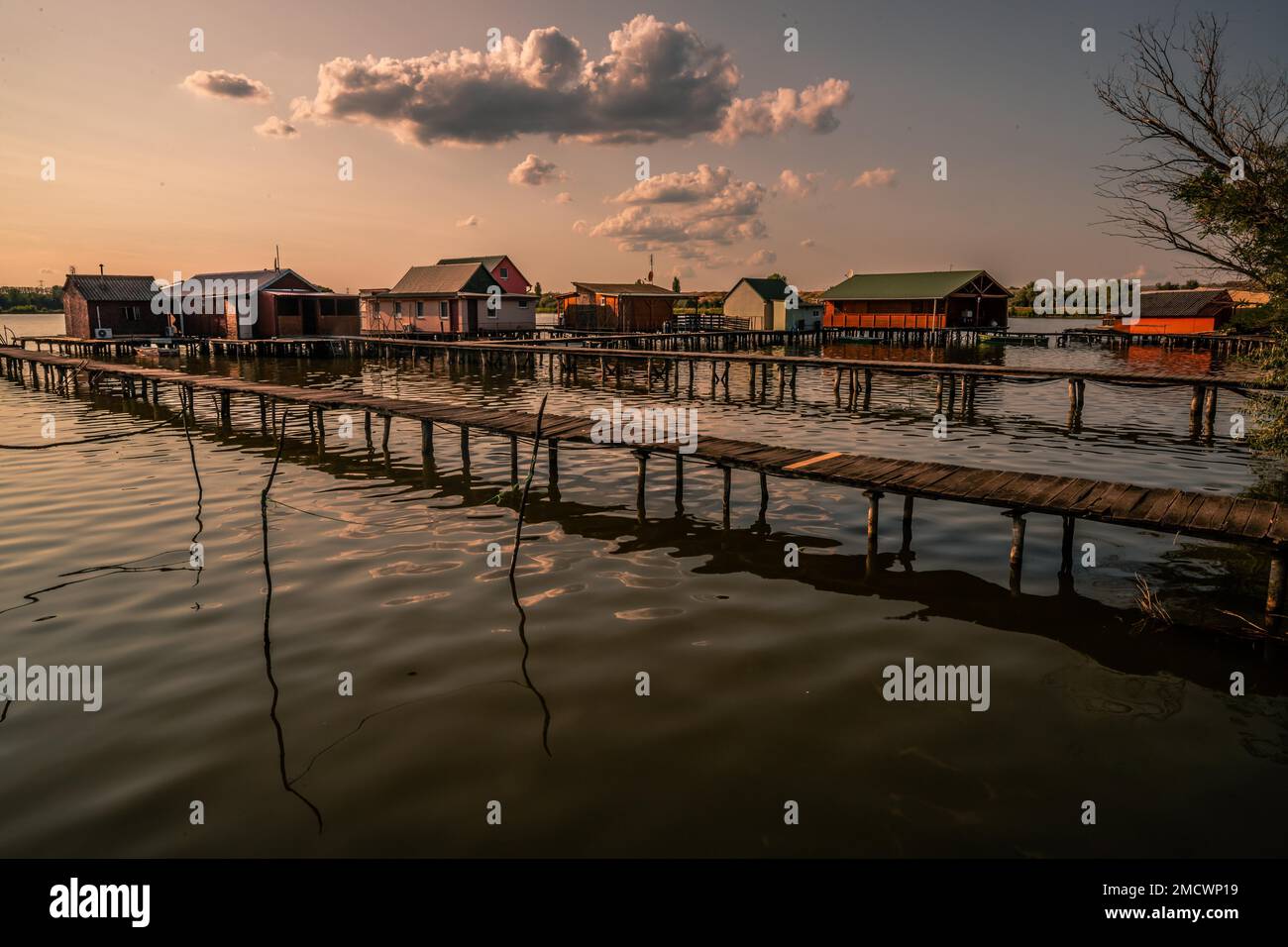 Kleine Holzhäuser mit einem Steg in einem See dienen als Angeln- und Ferienhäuser für Ungarn. Wunderschönes Landschaftsfoto bei Sonnenuntergang, Lake Bokodi Stockfoto