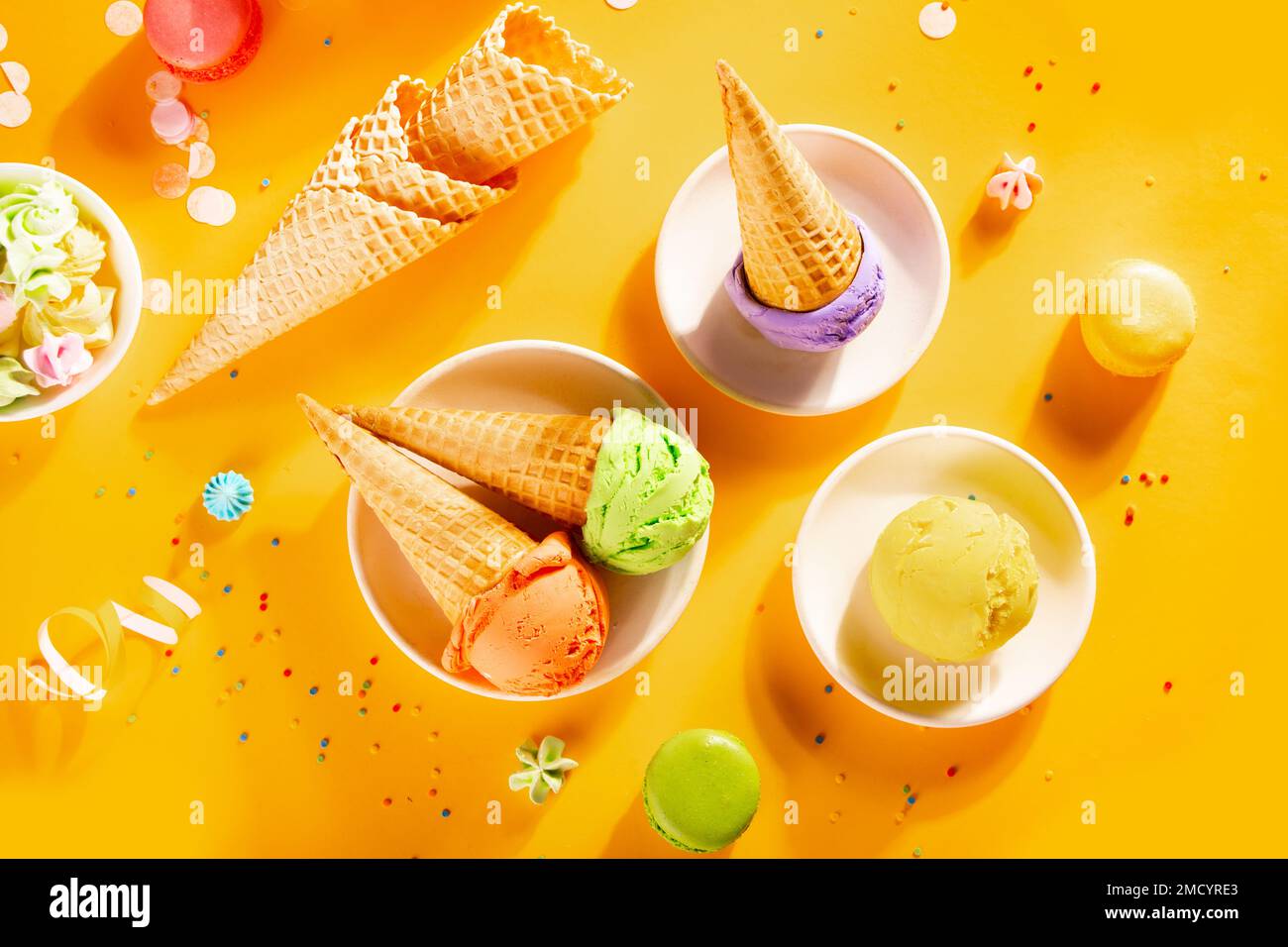 Verschiedene bunte Eislöffel oder -Bälle mit Waffelmuscheln auf gelbem Hintergrund. Draufsicht Stockfoto