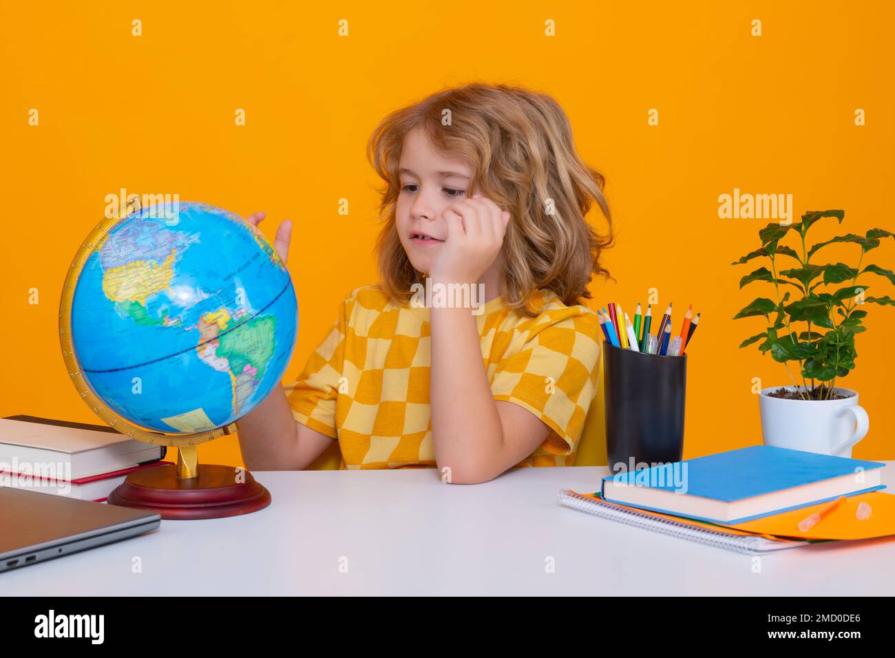 Schule und Bildungskonzept. Porträt eines süßen Schülers, der während des Geografie-Unterrichts auf dem gelben Studiohintergrund auf den Globus blickt. Zurück zu Stockfoto