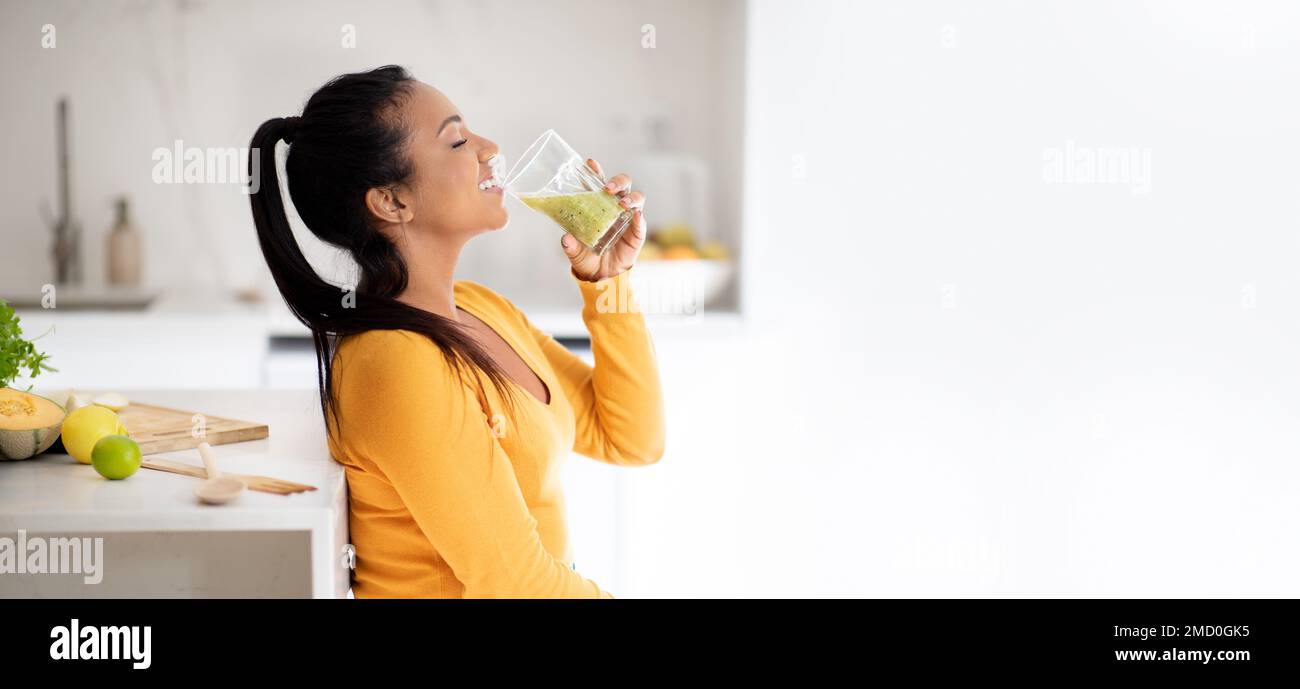 Glückliche junge afroamerikanische Veganerin am Tisch mit Bio-Gemüse, trinkt frischen Smoothie im Glas Stockfoto