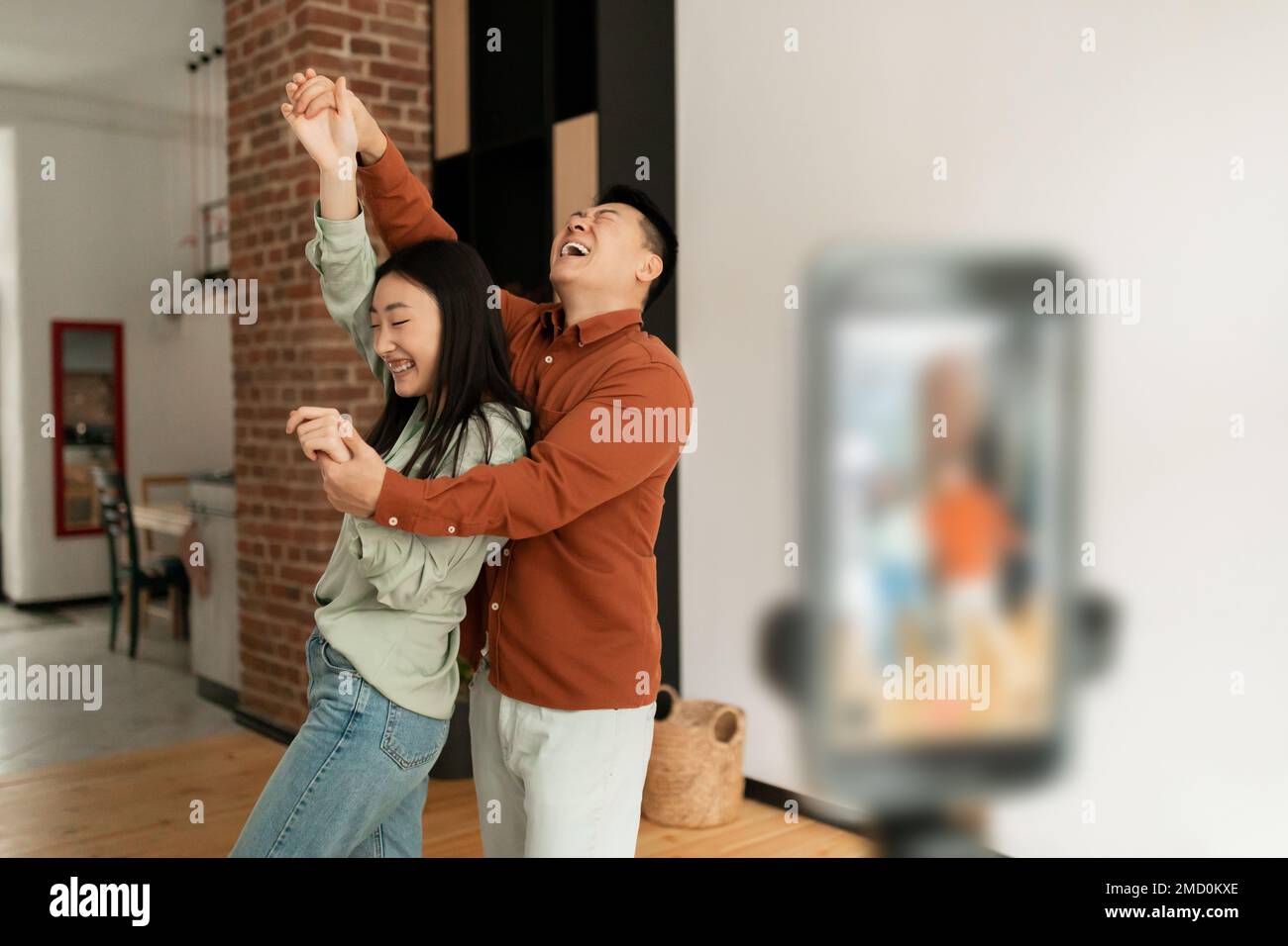 Verspielte asiatische Ehepartner übertragen oder zeichnen Inhalte auf, während sie vor der Smartphone-Kamera tanzen, Kopierbereich Stockfoto