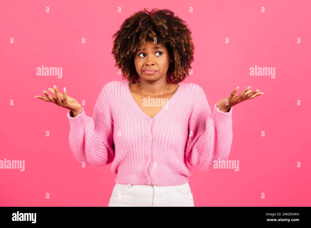 Unsichere, verwirrte, unfähige afroamerikanische lockige Dame spreizt ihre Arme an die Seiten Stockfoto