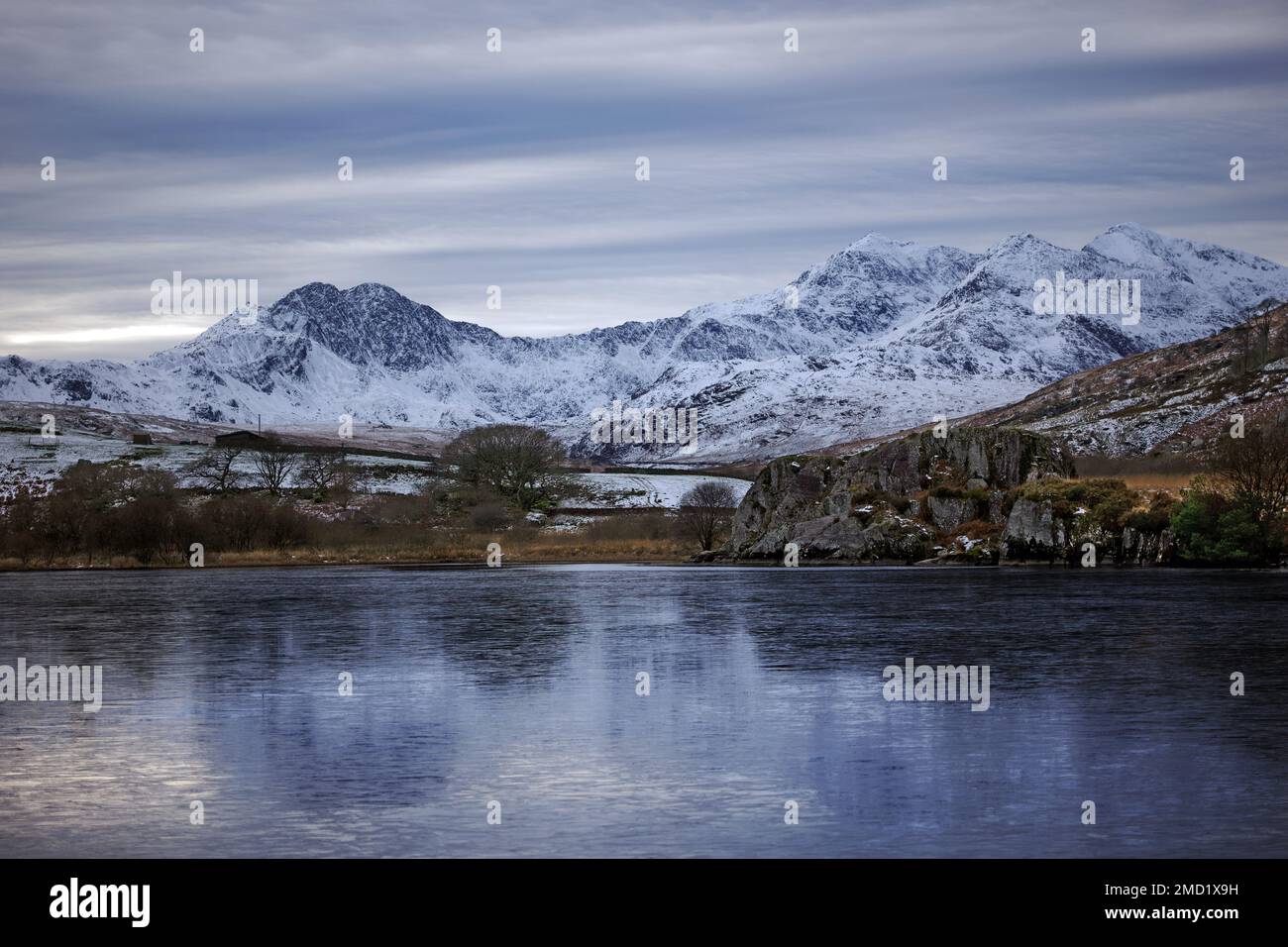 Mount Snowdon ist hier auf der anderen Seite des gefrorenen Sees von Llynnau Mymbyr im Tal von Dyffryn Mymbyr im Snowdonia-Nationalpark, Nordwales zu sehen. Stockfoto