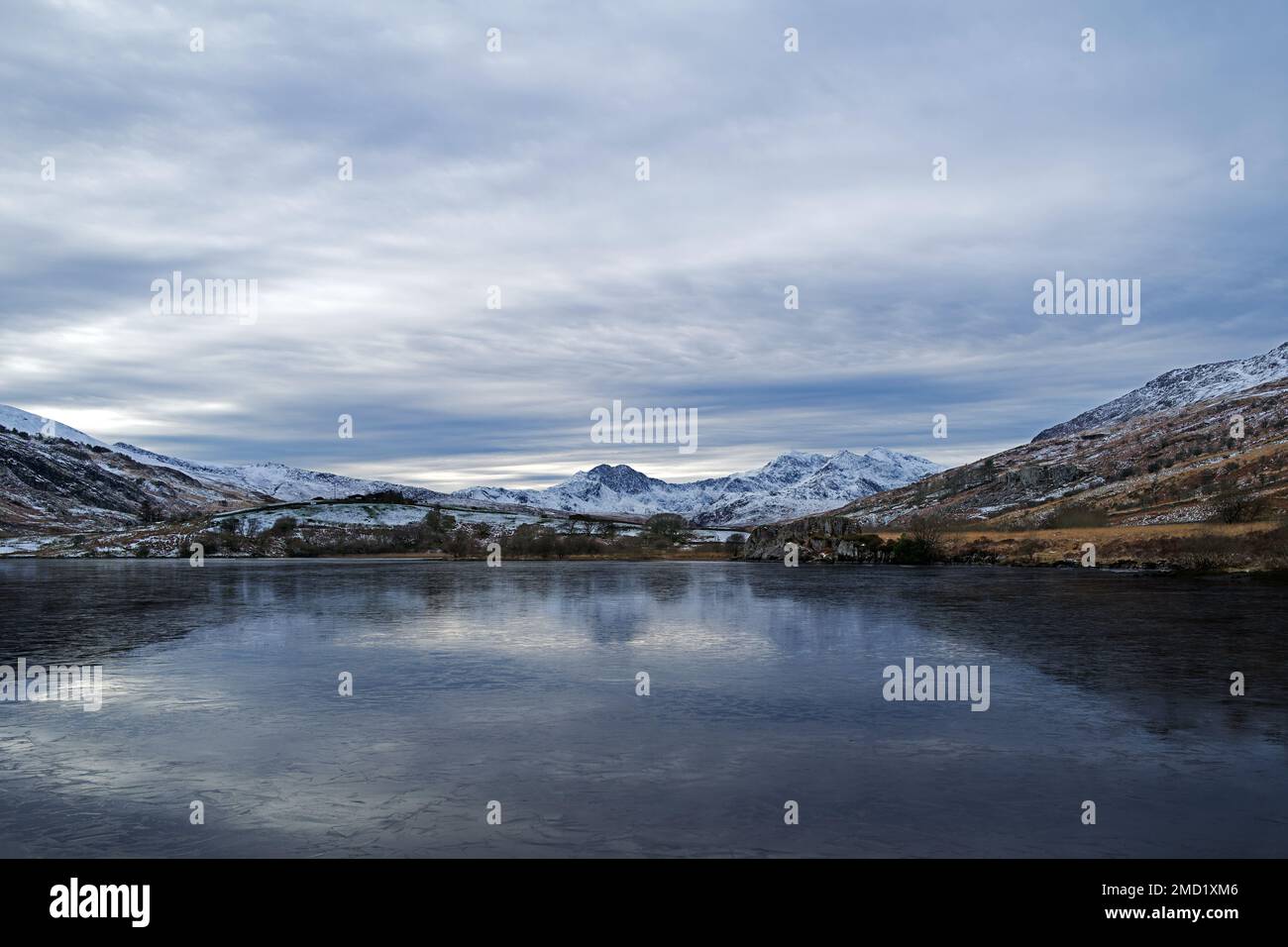 Mount Snowdon ist hier auf der anderen Seite des gefrorenen Sees von Llynnau Mymbyr im Tal von Dyffryn Mymbyr im Snowdonia-Nationalpark, Nordwales zu sehen. Stockfoto