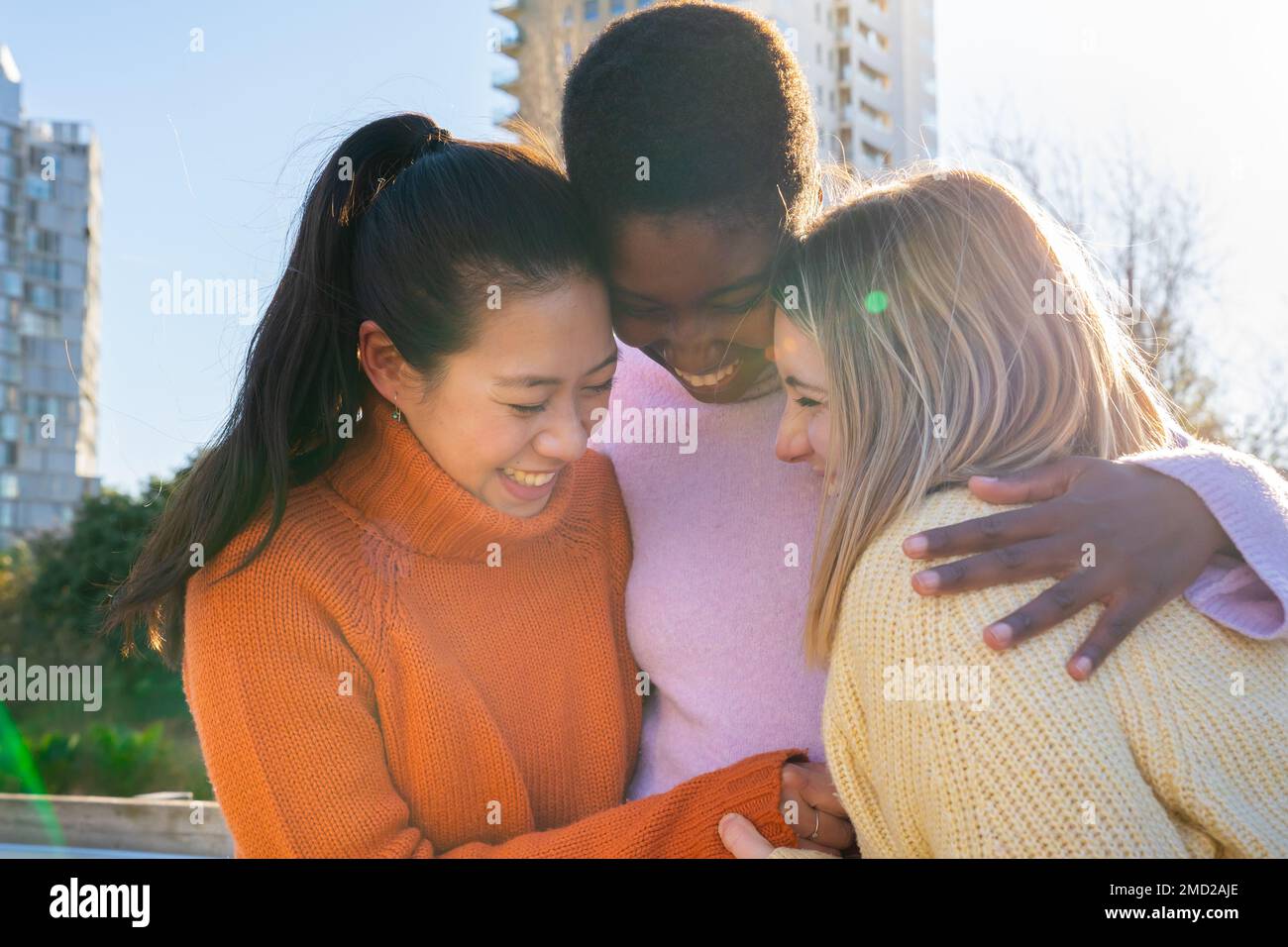 Drei Freundinnen umarmen sich liebevoll, haben Spaß zusammen, lachen glücklich und lächeln. Stockfoto