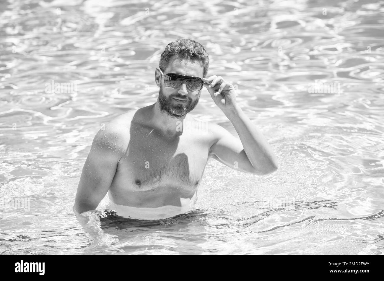 Glücklicher bärtiger Mann in einer Brille, der im Sommer im Pool schwimmt, entspannen Sie sich Stockfoto