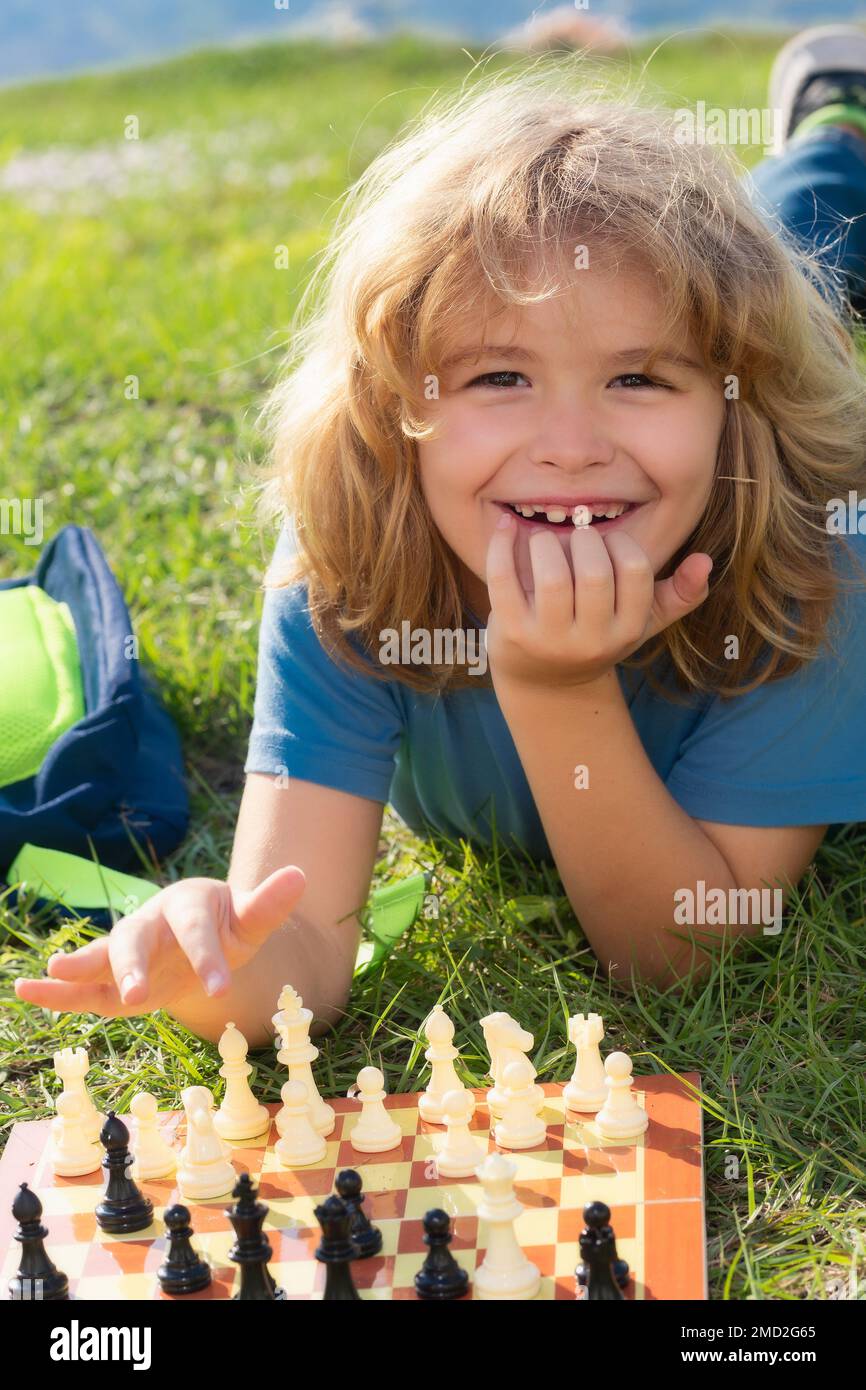 Kleiner Junge spielt Schach im Park. Ein Junge, der draußen Brettspiele spielt. Denk-Kind-Brainstorming und Idee im Schachspiel. Stockfoto