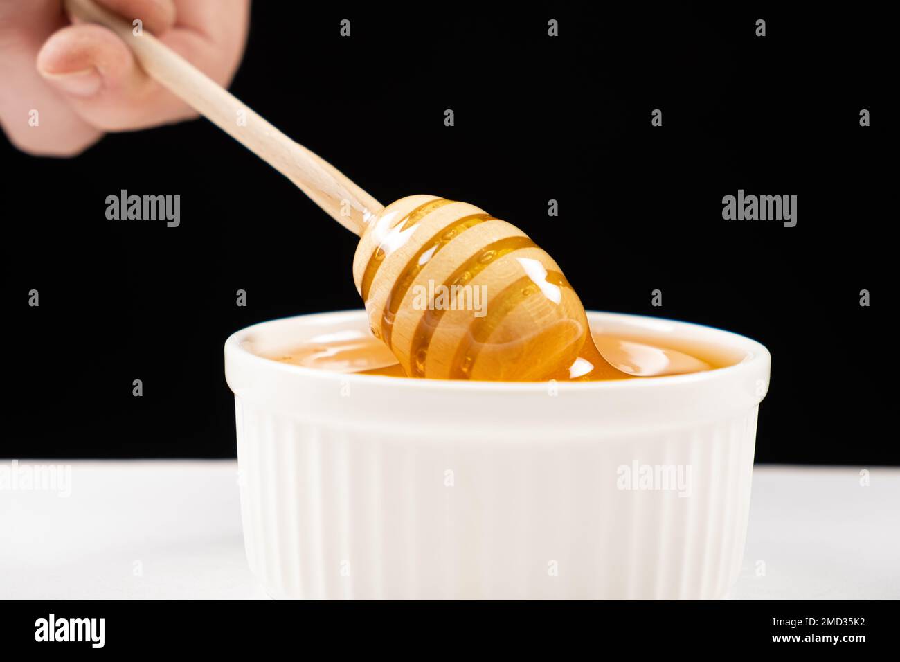Honig in einer weißen Keramikschüssel mit einem Holzlöffel auf schwarzem Hintergrund. Stockfoto