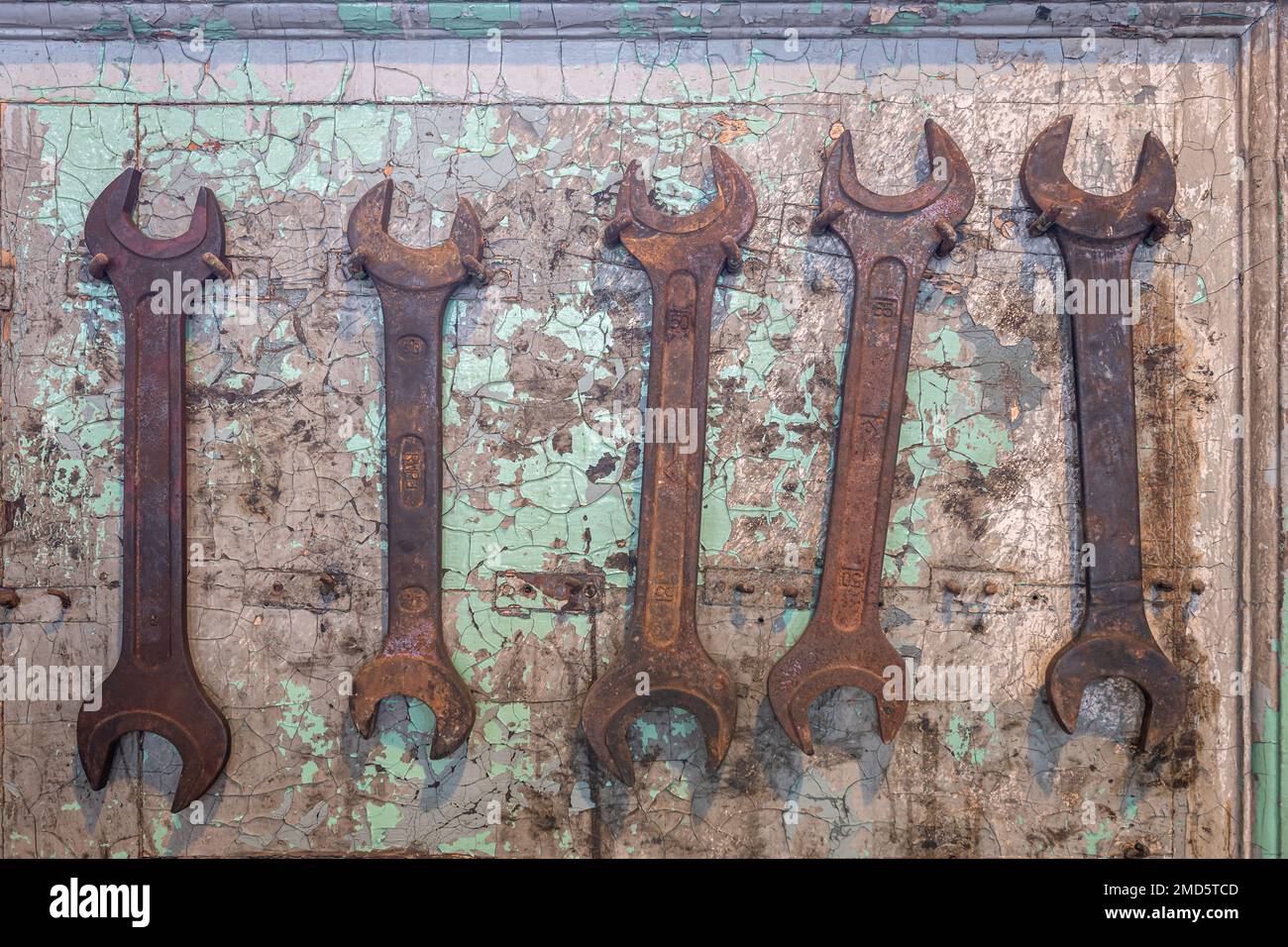 Fünf alte, verrostete Schlüsselwerkzeuge hängen an Nägeln an einer gerissenen, beschädigten Wand. Stockfoto