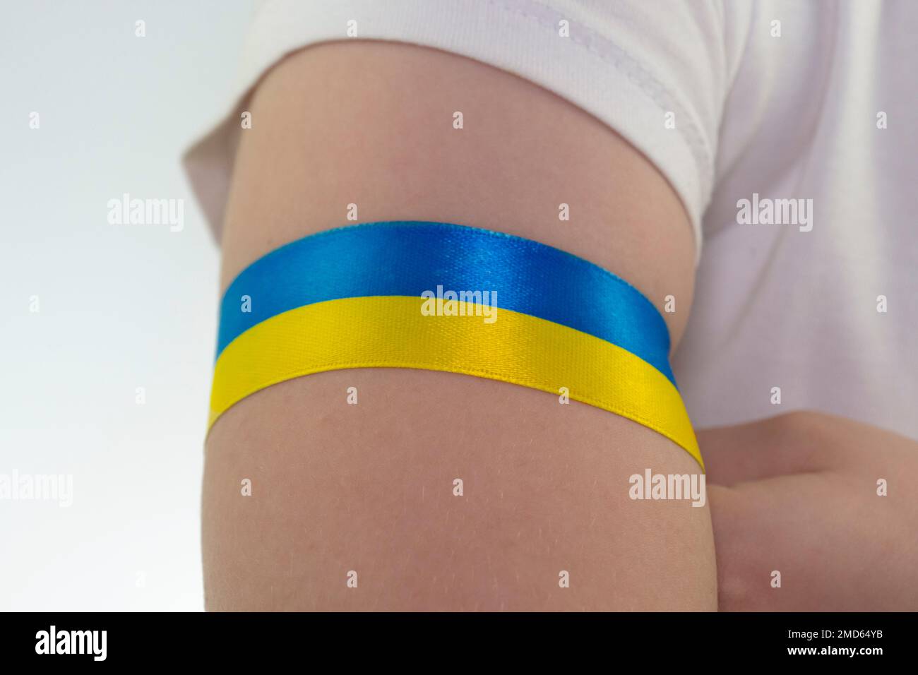 Ein Mädchen in einem weißen T-Shirt bindet ein gelb-blaues Textilband an ihren Unterarm (Nahaufnahme). Staatsflagge der Ukraine. Nationales Symbol der Ukraine. Patriot Stockfoto