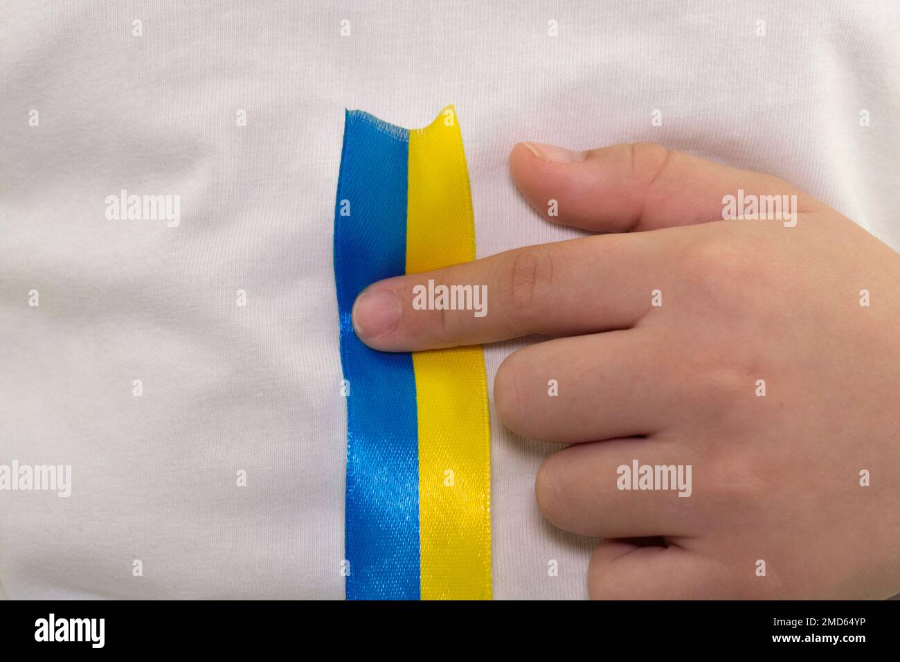 Ein Mädchen in einem weißen T-Shirt drückt mit dem Finger auf ein gelb-blaues Textilband. Staatsflagge der Ukraine. Nationales Symbol der Ukraine. Patriot. Nahaufnahme Stockfoto