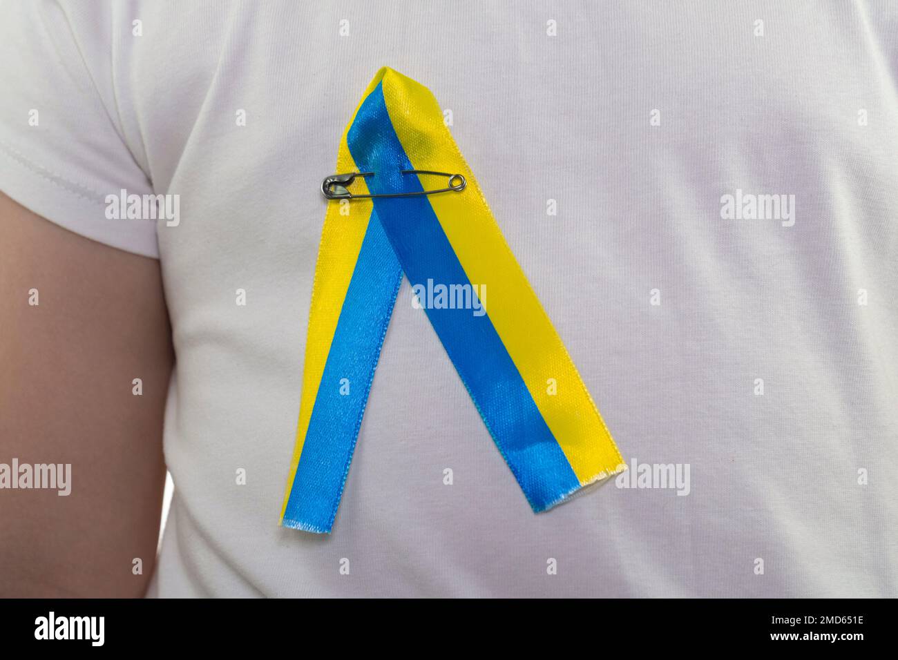 Mädchen in einem weißen T-Shirt mit einer Schlaufe aus gelb-blauem Textilband (Nahaufnahme). Staatsflagge der Ukraine. Nationales Symbol der Ukraine. Patriot Stockfoto