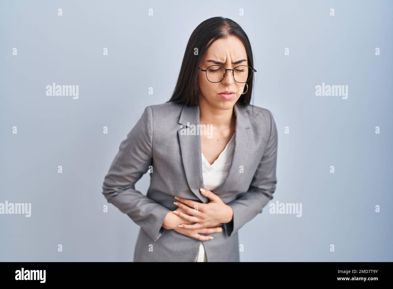 Hispanische Geschäftsfrau, die eine Brille mit der Hand auf dem Bauch trägt, weil Übelkeit, schmerzhafte Krankheit Unwohlsein. Ache-Konzept. Stockfoto
