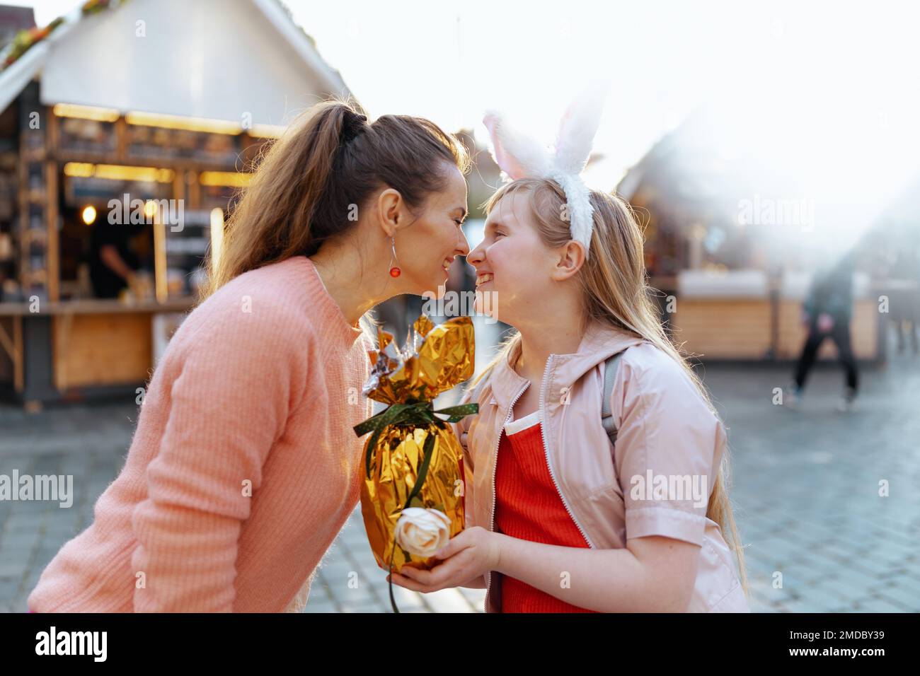 Osterspaß. Lächelnde moderne Mutter und Kind mit goldenem osterei auf dem Jahrmarkt in der Stadt. Stockfoto