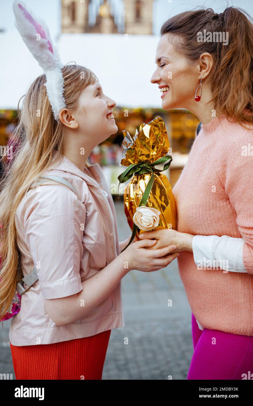 Osterspaß. Lächelnde moderne Mutter und Kind mit goldenem osterei auf dem Jahrmarkt in der Stadt. Stockfoto