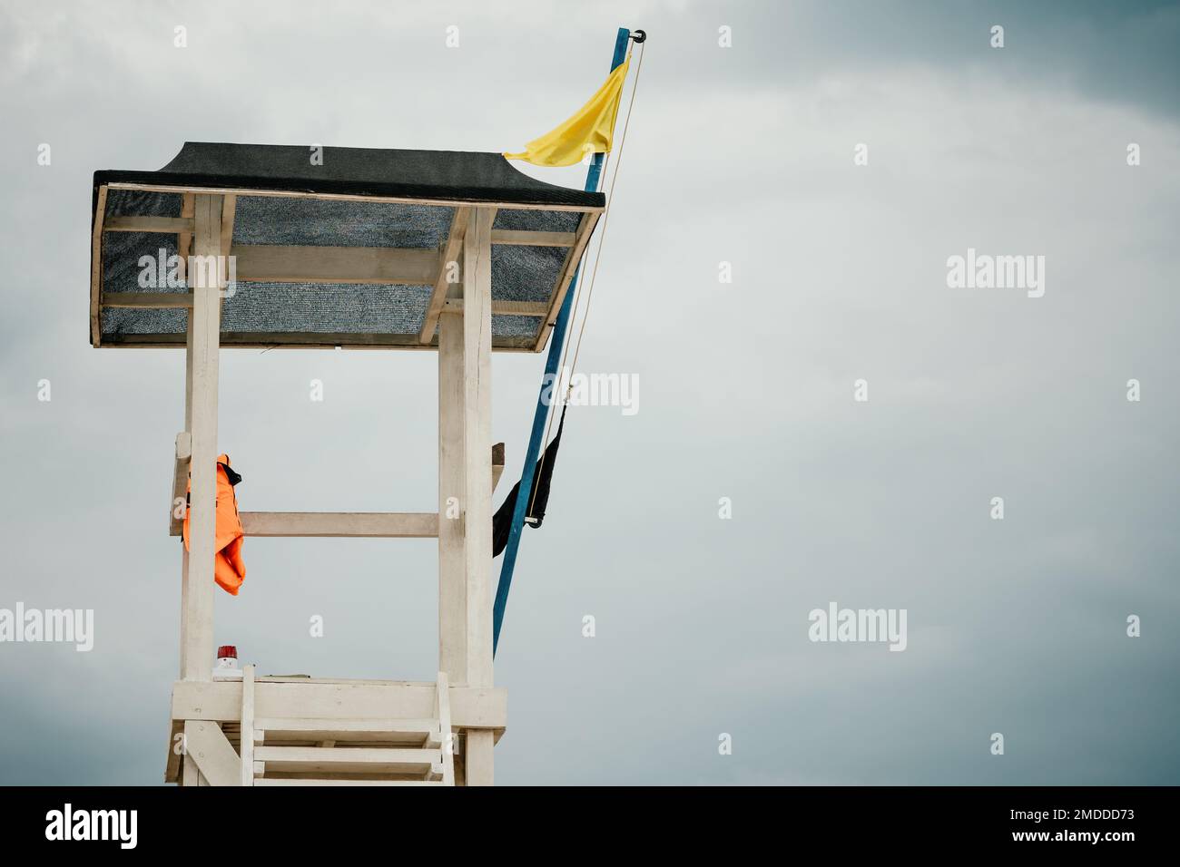 Leerer weißer Rettungsschwimmturm mit gelber Flagge am Strand bei windigem Wetter. Strandschwimmturm mit gelber Flagge. Niemand. Feiertage Stockfoto