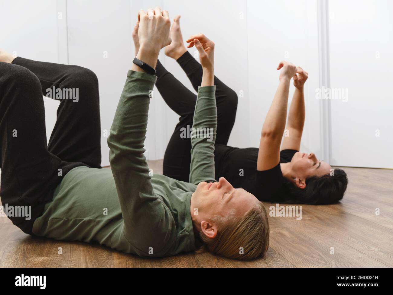 Rehabilitationsübungen. Physikalisches Therapiekonzept. Zwei Personen, die mit erhobenen Händen und Beinen auf dem Boden liegen, verbessern die Lymphe und den Blutfluss Stockfoto