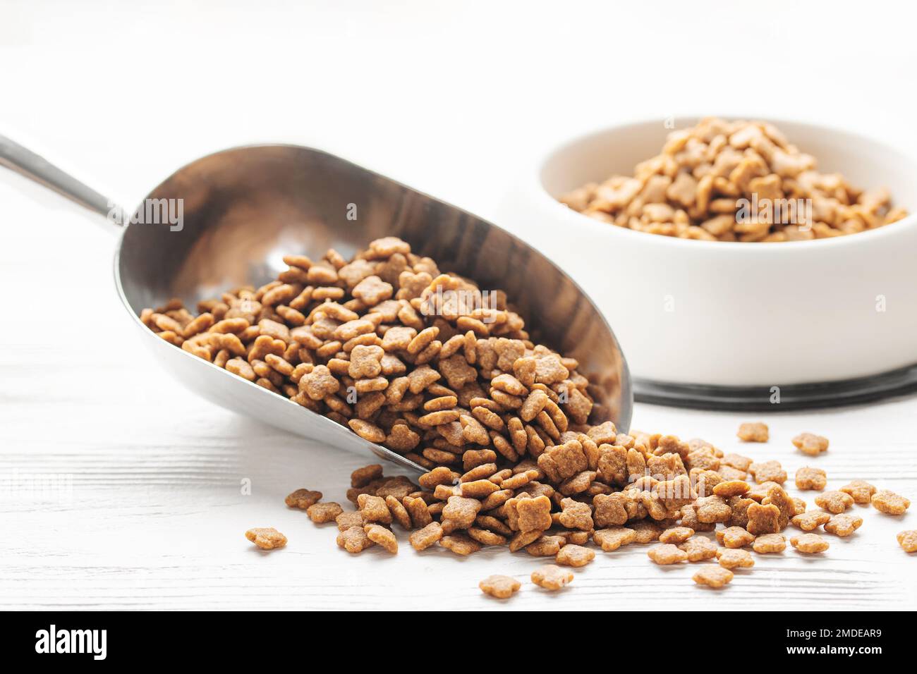 Trockenes Heimtierfutter. Trockenes Kibble-Food in einer Schaufel auf weißem Holzhintergrund Stockfoto