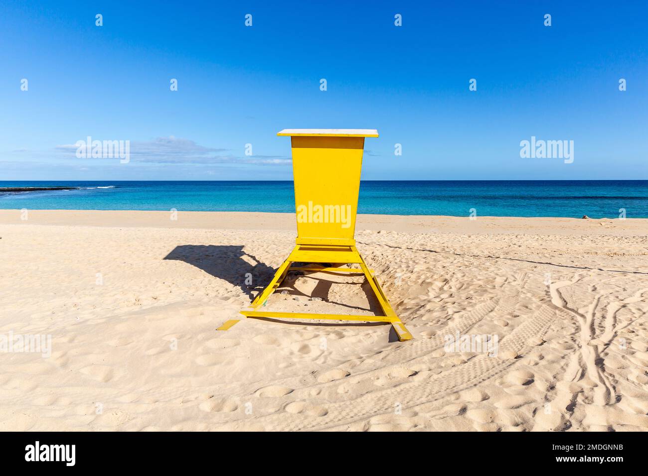 Hellgelbe Rettungsschwimmerkabine, die sich vor einem intensiven blauen Horizont erhebt. Stockfoto